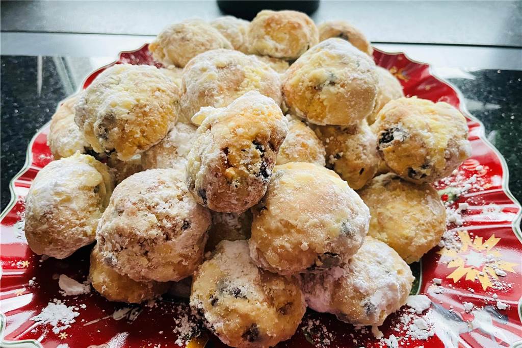 Angie backt Stollenkonfekt: Perfektes Gebäck für einen Adventsbrunch Das fertige Stollenkonfekt mit Puderzucker liegt auf einem roten Weihnachtsteller.