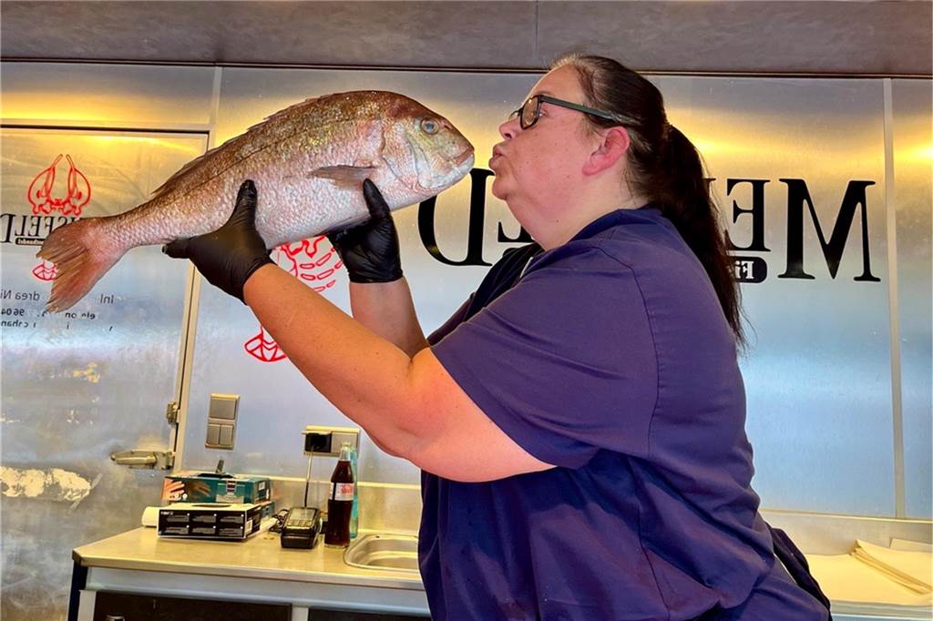 Andrea (53) ist Dortmunder Urgestein vom Wochenmarkt: „Wir brauchen ganz sicher keinen Kerl.“ Andrea Niesel hält in ihrem Fischstand auf dem Dortmunder Wochenmarkt einen Fisch in der Hand und deutet an, ihn küssen zu wollen.