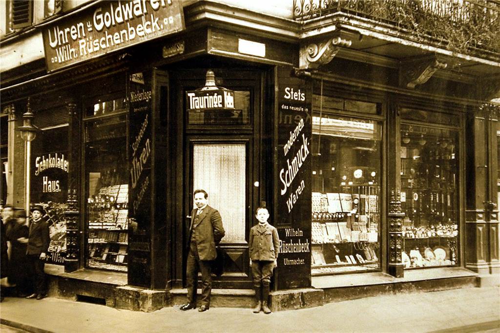 Wie der Juwelier Rüschenbeck zu einem der größten Schmuckhändler Europas wurde So sah das erste Juweliergeschäft der Familie Rüschenbeck an der Reinoldistraße aus. Wilhelm Rüschenbeck, der Großvater von Gerhard Rüschenbeck, hat es 1904 eröffnet. Er steht auf dem Bild vor der Eingangstür. Wer das Kind neben ihm ist, ist nicht mehr überliefert.