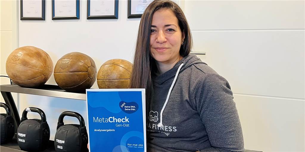 Fitnesstrainerin Soraya Dünninghaus hält eine Mappe der MetaCheck Gen-Diät hoch.