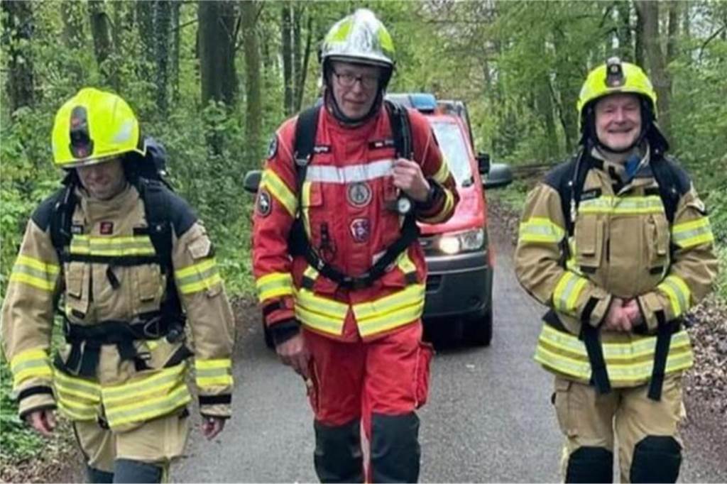 Drei Feuerwehrmänner laufen durch einen Wald. 