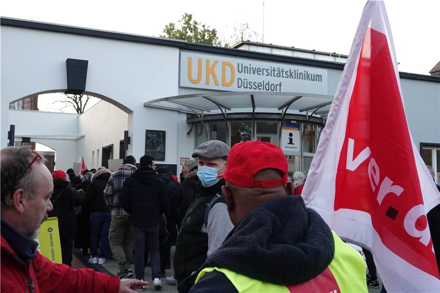 „Erhebliche Einschränkungen“ an Unikliniken in NRW: Operationen wegen Warnstreiks abgesagt Streikende stehen vor dem Eingang der Uniklinik Düsseldorf und schwenken Fahnen.