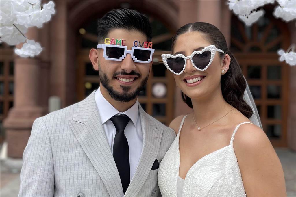 Antrag vor Apple Store: Harun und Sümeyye haben in Dortmund geheiratet Das Brautpaar hat Sonnenbrillen auf. Sümeyye eine Brille mit Gläsern in Herzform und einem weißen Rahmen. Harun eine eckige Brille mit dem bunten Schriftzug „Game over“ auf seiner Stirn.