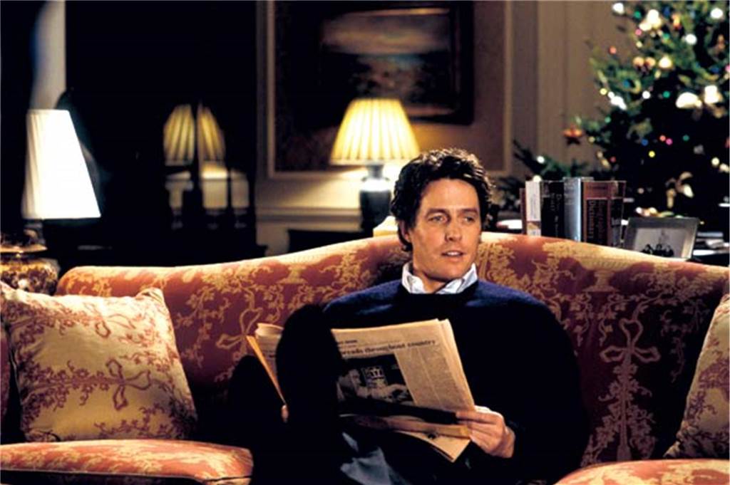 Schauspieler Hugh Grant sitzt auf einem Sofa.