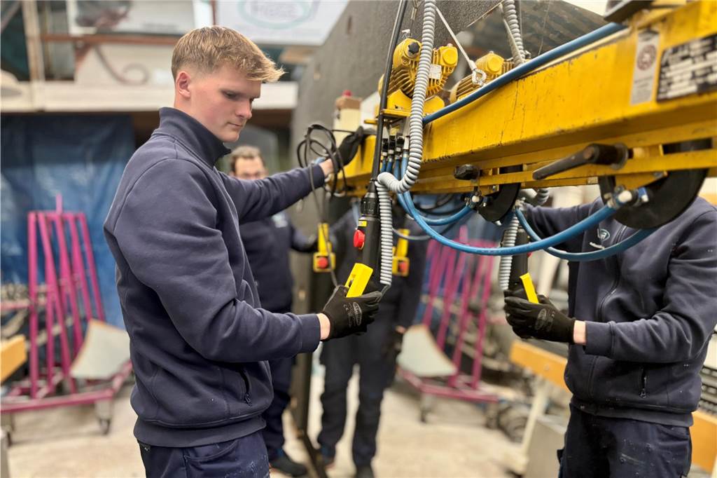 Teamarbeit: Marlon Malecha und seine Kollegen heben mithilfe einer Maschine eine große Glasscheibe durch die Produktionshalle am Westring.