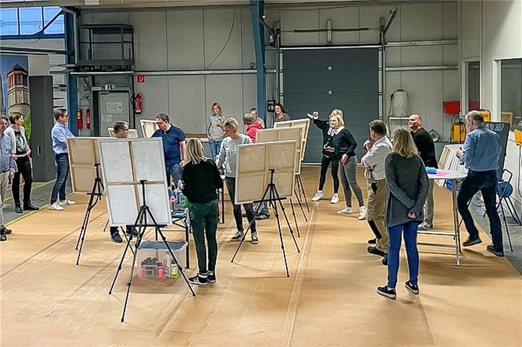 Alexa Terfrüchte macht Stammtische und Firmenbelegschaften kreativ Tenbrink-Mitarbeiter an Staffeleien in einer Werkshalle.