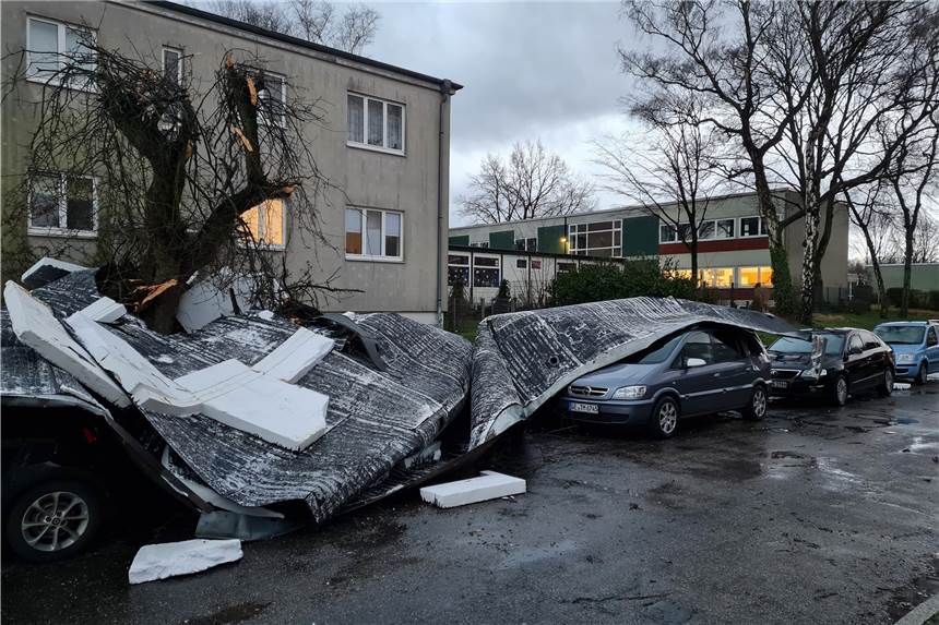 Teile eines vom Sturm Ylenia abgedeckten Flachdaches liegen auf einer Straße und auf geparkten Autos.