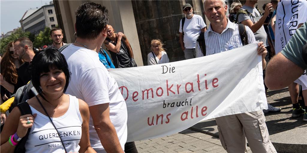 Rechtsextreme hoffen auf den Krisengewinn: Droht im Herbst eine Energiepreis-Protestwelle? Teilnehmer der Demonstration "Uneingeschränkte Wiederherstellung sämtlicher Grundrechte" stehen mit einem Transparent mit der Aufschrift "Die Demokratie braucht uns alle" am Brandenburger Tor.