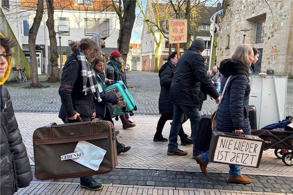 Teilnehmer marschieren an der Kirche vorbei. Einige tragen Koffer mit Aufschriften, welche zum erinnern aufrufen