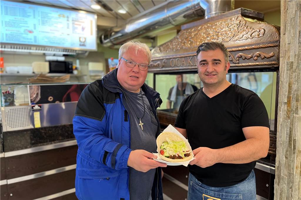 Thomas Frauendienst lädt 100 Menschen zum Essen ein - das steckt dahinter Thomas Frauendienst (l.) und Selam Tasdemir stehen vor einem Grill und halten einen Teller mit einer Dönertasche in den Händen.