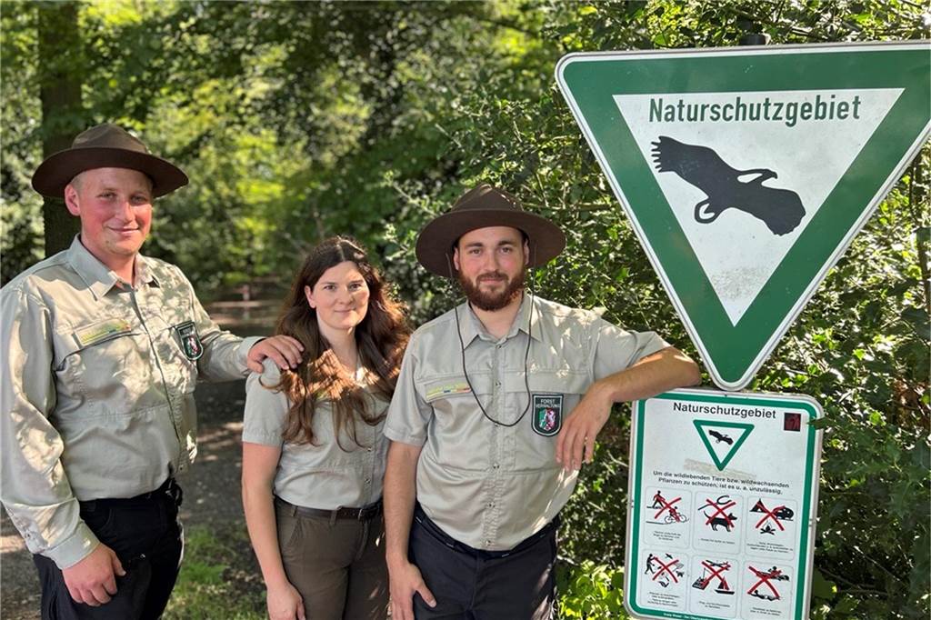 Ein Blick durch die Fenster des wilden Waldes in Schermbeck Drei Menschen an einem Schild im Wald