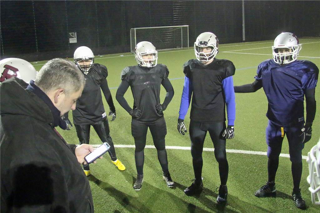 Warum Jens Mumm den Super Bowl verpasst, obwohl er glühender Fan ist Trainer Phil Wennker guckt sich die Spielzüge auf dem Handy an. Jens Mumm (3.v.r.) hört zu.