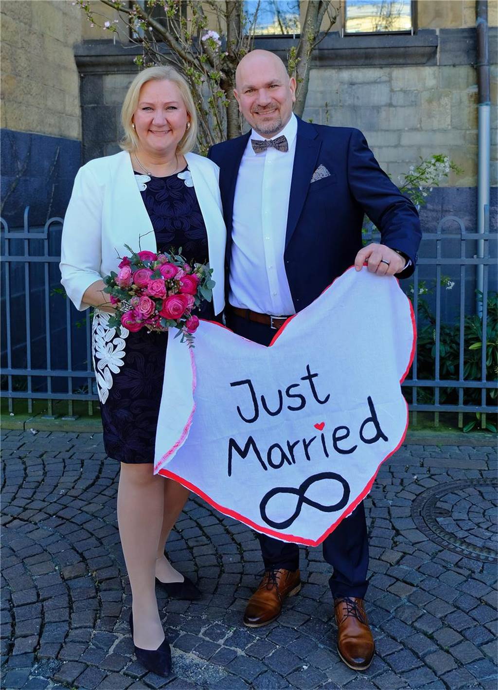 Das frisch vermählte Ehepaar Martina Elies und Alexander Kuhs steht vor dem Rathaus Recklinghausen. In den Händen halten beide ein aus weißem Stoff ausgeschnittenes Herz, auf dem in schwarzer Schrift Just Married steht.