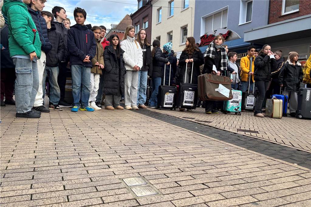 Teilnehmer vom Marsch stehen in einer Reihe. Menschen mit Koffern und Schildern sind zusehen. 