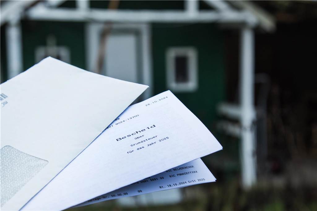Grundsteuer: Bürger zahlt nun 1000 Prozent mehr für Doppelhaushälfte Ein Brief mit einem Grundsteuerbescheid vor einem Haus.