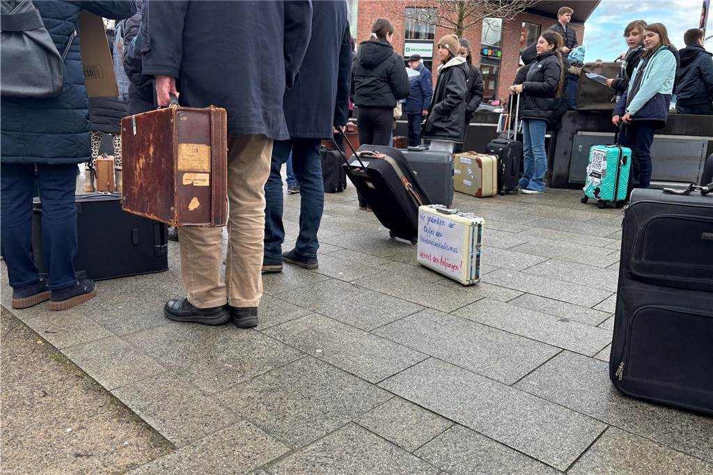 Mehrere, teilweise beschriftete Koffer stehen auf dem Boden. Die Schriften rufen zum Gedenken an den Holocaust auf. 