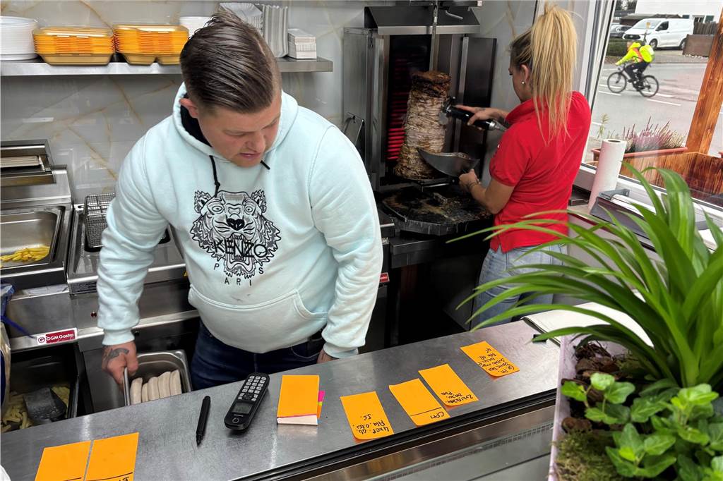 Timur Ratzer steht hinter der Theke und nimmt Bestellungen an, während Dimitra Georgiou Fleisch vom Gyros-Spieß abschneidet.