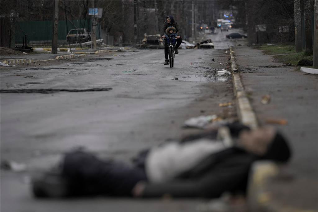 Ein Jahr Krieg in der Ukraine: Diese Orte und Geschehnisse sind besonders in Erinnerung geblieben Ein Mann und ein Kind fahren auf einem Fahrrad, während die Leiche eines Zivilisten auf der Straße im ehemals russisch besetzten Kiewer Vorort Butscha liegt.