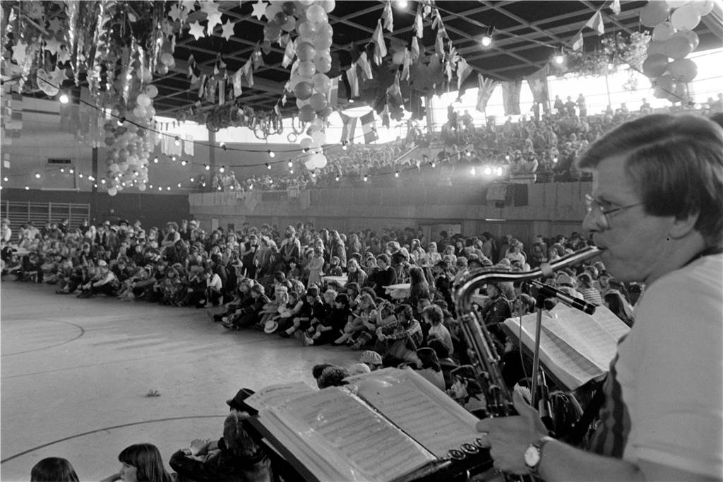 Menschen sitzen an Karneval in einer Turnhalle.