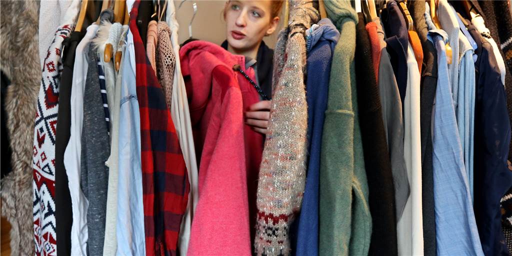 Acht Tipps, die Ihre Kleidung und das Klima schonen Eine Frau stöbert in ihrem vollen Kleiderschrank.