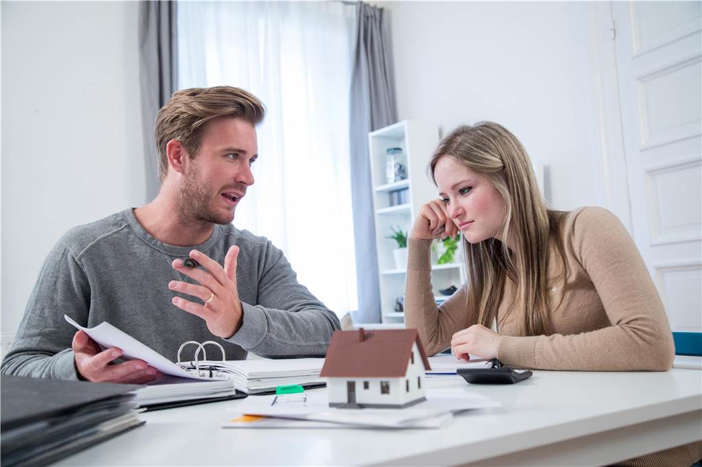 Grundsteuerbescheide kommen bald: Das müssen Hausbesitzer jetzt wissen Ein Mann und eine Frau sitzen an einem Tisch und prüfen Grundsteuer-Unterlagen. Davor steht ein Miniaturhaus.