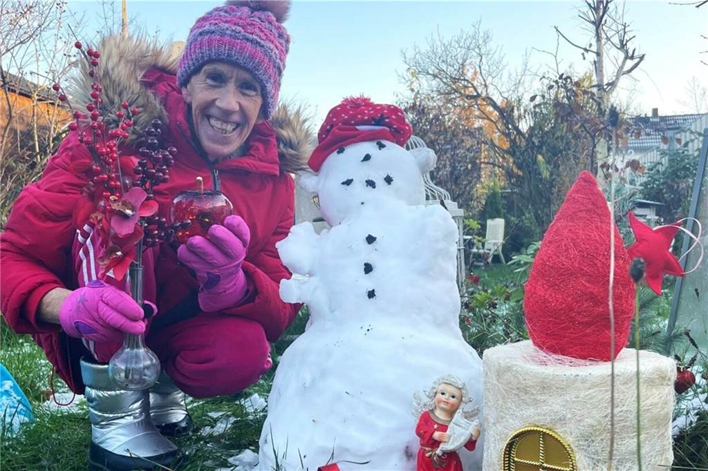 Ein 65-jähriger Mann mit Mütze und Skijacke hockt neben einem Schneemann. Es ist Winter,