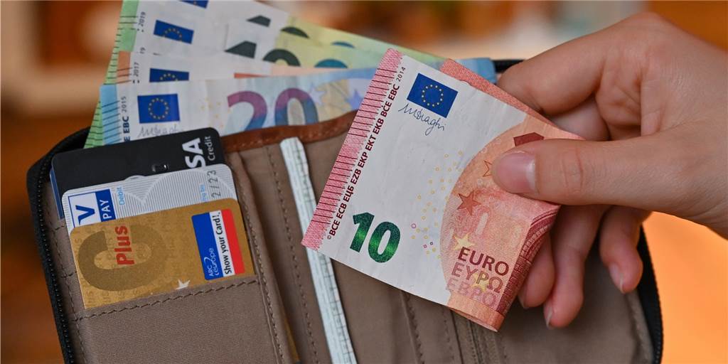 Gehalt seit 1999: So viel verdienen die Werner - es gibt einen Haken Jemand steckt einen Schein in ein Portemonnaie