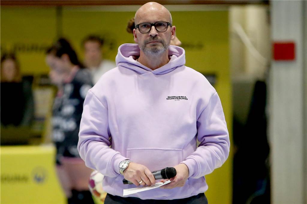 Rupert Thiele steht in einer Sporthalle mit einem Mikrofon in der Hand.