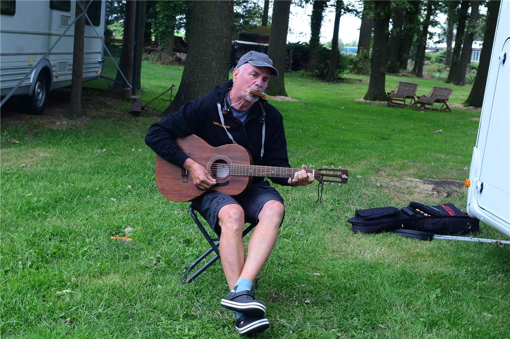 Mini-Campingplatz hat eigenen Charme: Camper genießen Ruhe und Radwege Wolfgang Schlüter sitzt vor seinem Wohnmobil auf einem kleinen Klappstuhl und spielt gleichzeitig Gitarre und Mundharmonika.