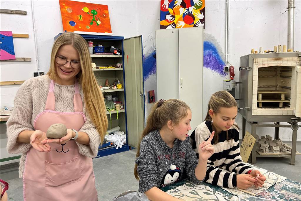 Töpferkurs für Kinder: Ukrainerin fördert die kreative Bildung Eine Frau hat eine Kugel Ton in der Hand. Neben ihr sitzen zwei Kinder am Tisch.