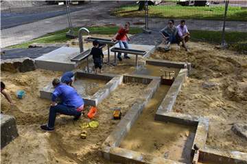 Zahlreiche Kinder und auch die Eltern spielen mit Wasser und Sand.