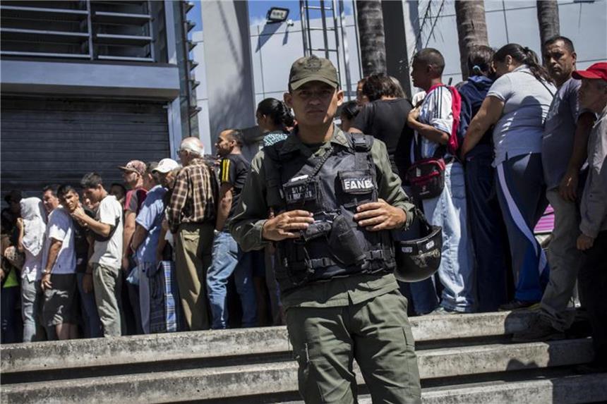 Plünderungen: Militär kontrolliert Supermärkte in Venezuela Zahlreiche Menschen stehen in Caracas stundenlang Schlange vor einem Lebensmittelladen, der von einem Polizisten bewacht wird. Foto: Rayner Pena