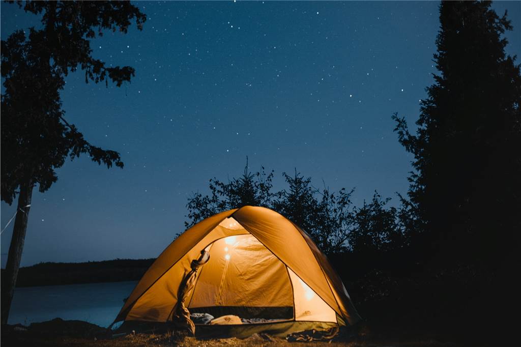 Naturnah, aber meist verboten - Wo wildes Zelten dennoch möglich ist Ein beleuchtetes Zelt steht nachts unter klarem Sternenhimmel in einem Wald an einem See.