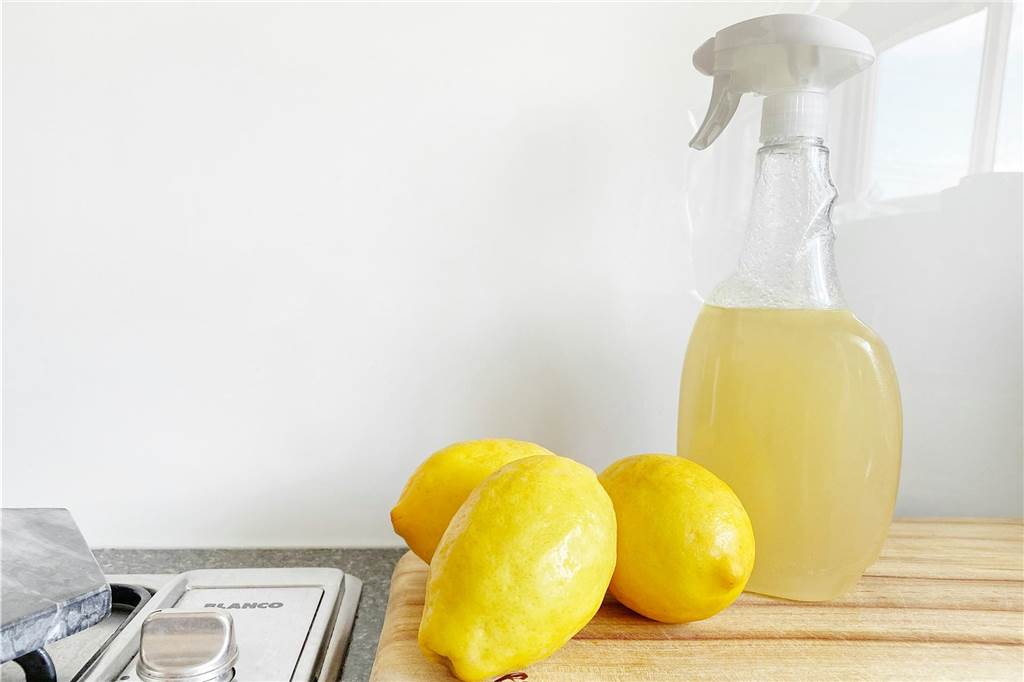 Kühlschrank reinigen: Hausmittel gegen Keime und Gerüche Auf einem Holzbrett liegen Zitronen und daneben steht eine Sprühflasche gefüllt mit Zitronensaft.