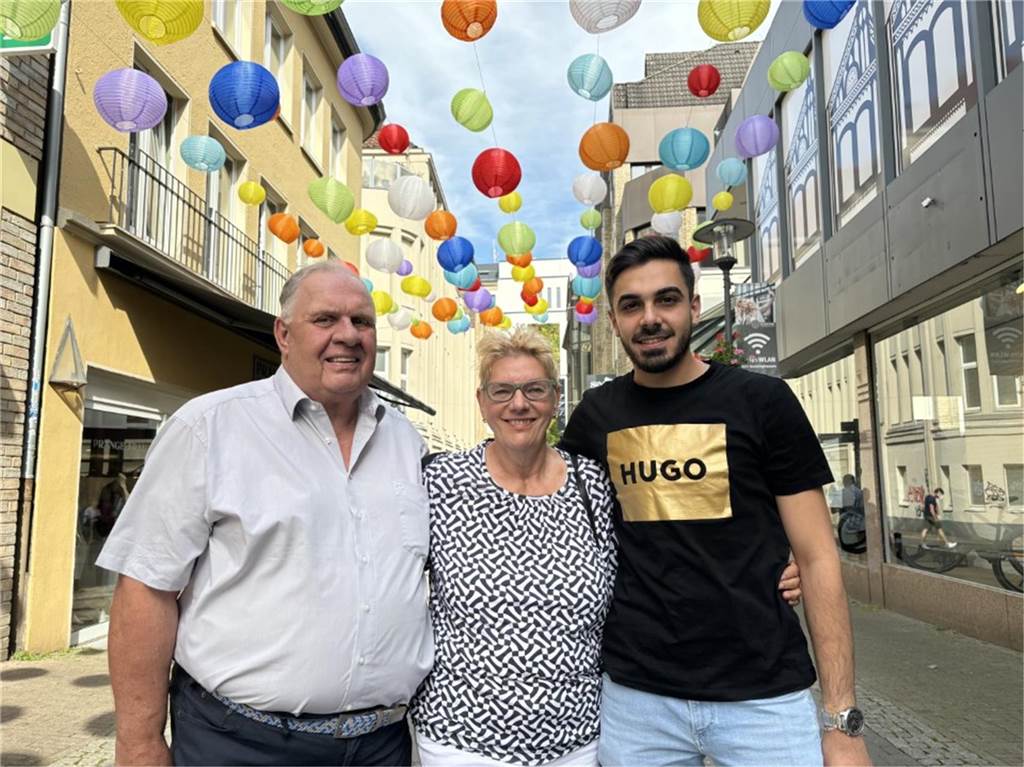 Von links nach rechts: Das Ehepaar Norbert und Angelika Schildgen steht mit dem Deutsch-Syrer Marwan Abazeid in der Fußgängerzone in der Innenstadt von Recklinghausen unter aufgespannten Lampions.