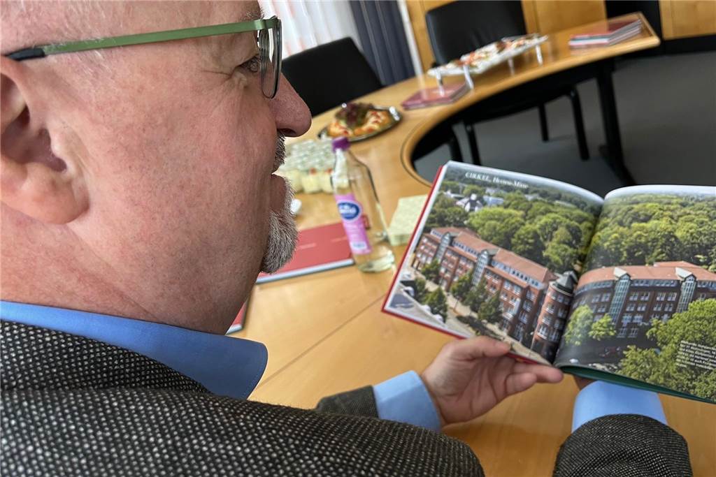 Buch zu 100 Jahren Schettler: Chef gibt Versprechen trotz Baukrise Ein Mann sitzt an einem Tisch und schaut sich in einem Buch das Foto eines großen Geschäftsgebäudes an.