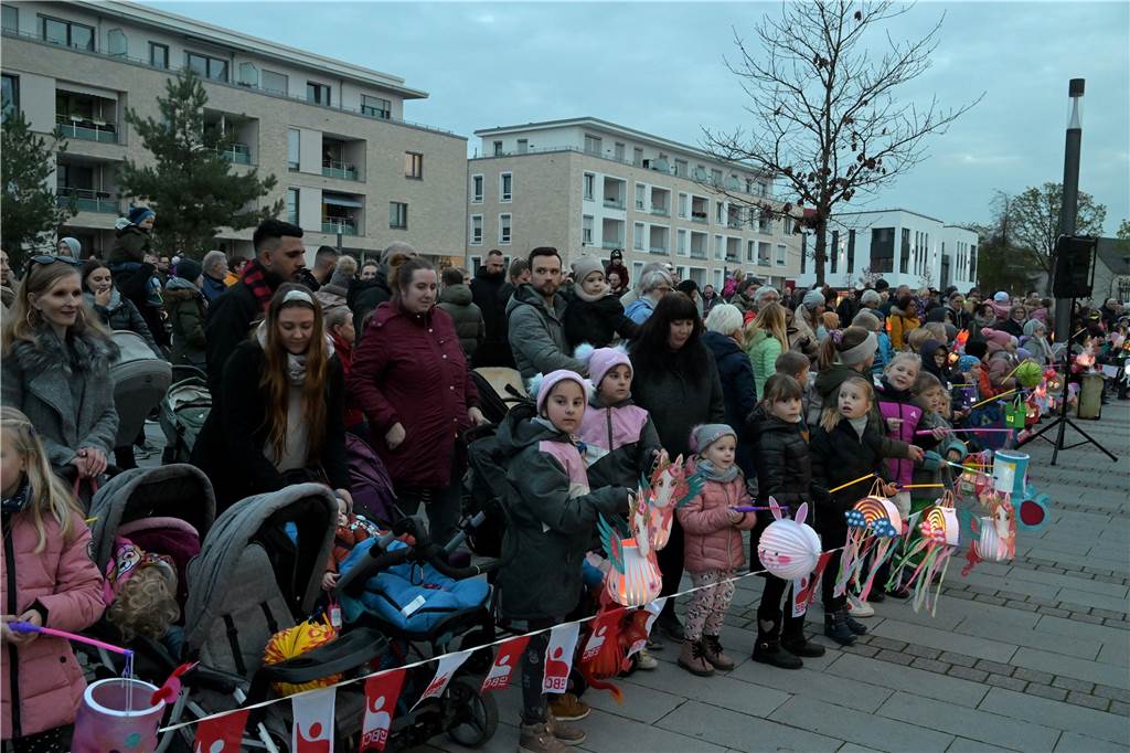 Viel Kinder mit Laternen stehen hinter einem Absperrband und halten Laternen in der Hand. Hinter ihnen stehen Erwachsene. 