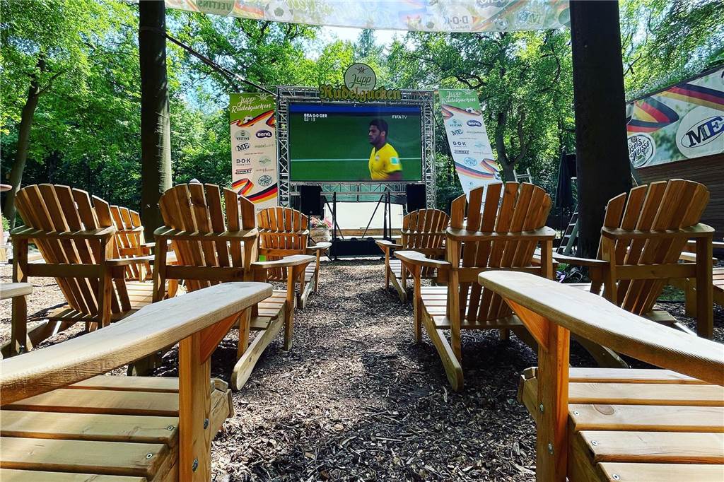 Jupps Biergarten umgekrempelt: „Machen auf, sobald die Sonne scheint“ Mehrere Stühle stehen in Jupps Biergarten in Haltern, im Hintergrund ist eine Leinwand zu sehen, auf der ein Fußballspiel gezeigt wird.