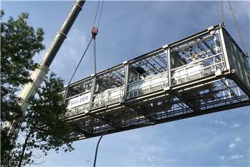 Zwei Autokräne heben die erste von zwei Teilanlagen von einem Kanalschiff auf einen Straßen-Schwertransporter.