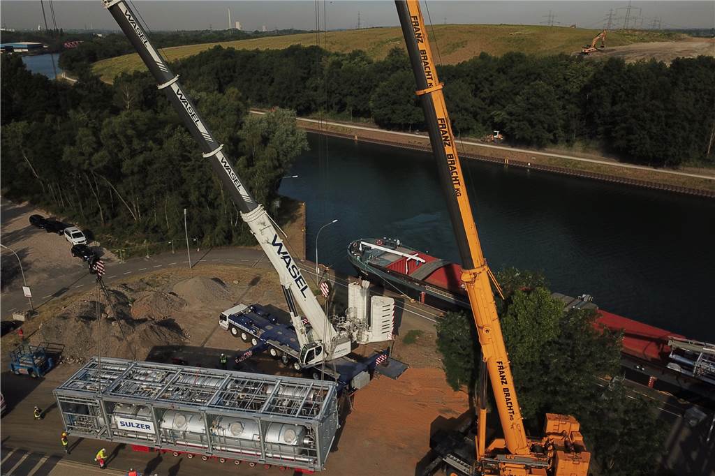 Wie zwei Stahl-Kolosse das Rütgers-Werk in eine neue Generation führen Zwei Autokrane heben die erste von zwei Teilanlagen von einem Kanalschiff auf einen Straßen-Schwertransporter.