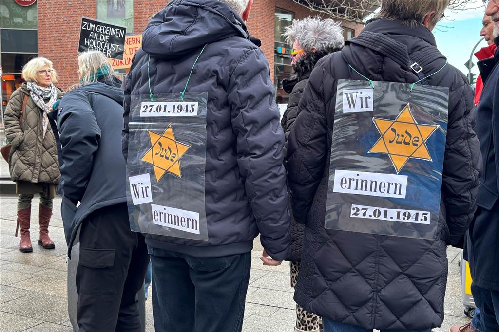 Zwei Teilnehmer tragen Schilder auf ihren Rücken. Die Schilder bilden einen Judenstern ab und rufen zum erinnern auf. sie wurden von hinten fotografiert. 