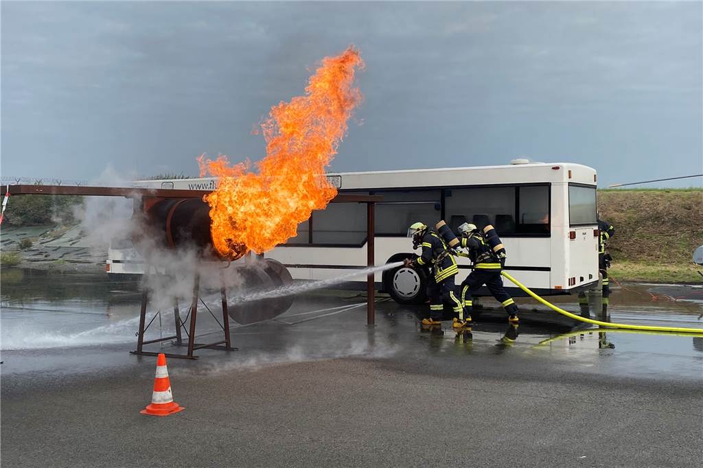 Zwei Feuerwehrleute löschen Flammen aus einem ausgebauten Triebwerk. Daran wird ein echter Brand simuliert.