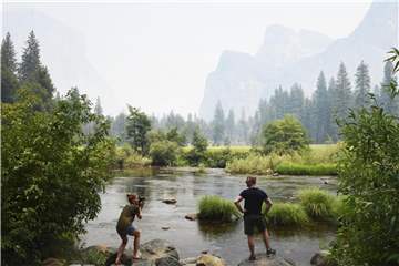 Zwei Touristen am Merced River im Yosemite-Tal, während Rauch im Hintergrund die Bergkulisse verschleiert. Foto: Eric Paul Zamora/The Fresno Bee/AP